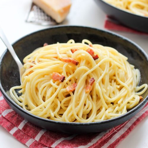 Macarrão a carbonara é minha receita de massa conforto, um clássico italiano que agrada todo mundo aqui em casa. Com poucos ingredientes você vai fazer uma receita maravilhosa de macarrão que fica pronta em 20 minutos. Eu amo essa receita em vários níveis e camadas diferentes, ela é simples de fazer, vai poucos ingredientes, rende super bem e fica pronta em poucos minutos. Se for uma pessoa mais experiente, com certeza consegue fazer no tempo de cozinhar o macarrão. A qualidade dos ingredientes importa E aqui mora um grande "truque” para que seu macarrão a carbonara não fique com aquele super gosto de ovo: use um bom queijo parmesão, ele é que vai tirar o gosto de ovo e dar mais sabor ao seu prato. Gosto de usar o Parmesão da Scala 12 ou 18 meses, eles são levemente frutados, com sabor encorpado e não precisa usar uma quantidade muito grande para conseguir o melhor resultado. Não faça carbonara (nem essa receita nem outra) com parmesão de pacotinho, ele tem pouco sabor, não derrete e o resultado vai ser completamente diferente do que você espera. Prefira e use somente queijo parmesão fresco, de preferência ralado na hora. Essa receita já vai poucos ingredientes, então minha dica é: use os melhores que tiver disponível. Os ovos também interferem no resultado final, prefira os caipiras com a gema bem amarela, aqui a diferença do caipira para o ovo branco é só na cor, o sabor não vai mudar muito. Mas o carbonara feito com ovo caipira fica muito mais bonito e amarelinho do que o carbonara feito com ovo branco. Sobre queijos, eu prefiro usar parmesão mesmo, mas os tradicionais dirão que carbonara deve ser feito com pecorino. Aqui mora um grande problema para nós brasileiros: quase não há oferta de queijo pecorino, é difícil de achar e muito caro. Por esse motivo eu faço com parmesão de boa qualidade, boa maturação que o resultado é um macarrão a carbonara cremoso e que cabe no nosso bolso.